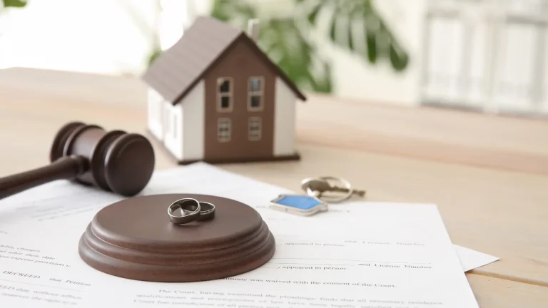 Divorce concept with wedding rings, a gavel, and a model house on legal documents.